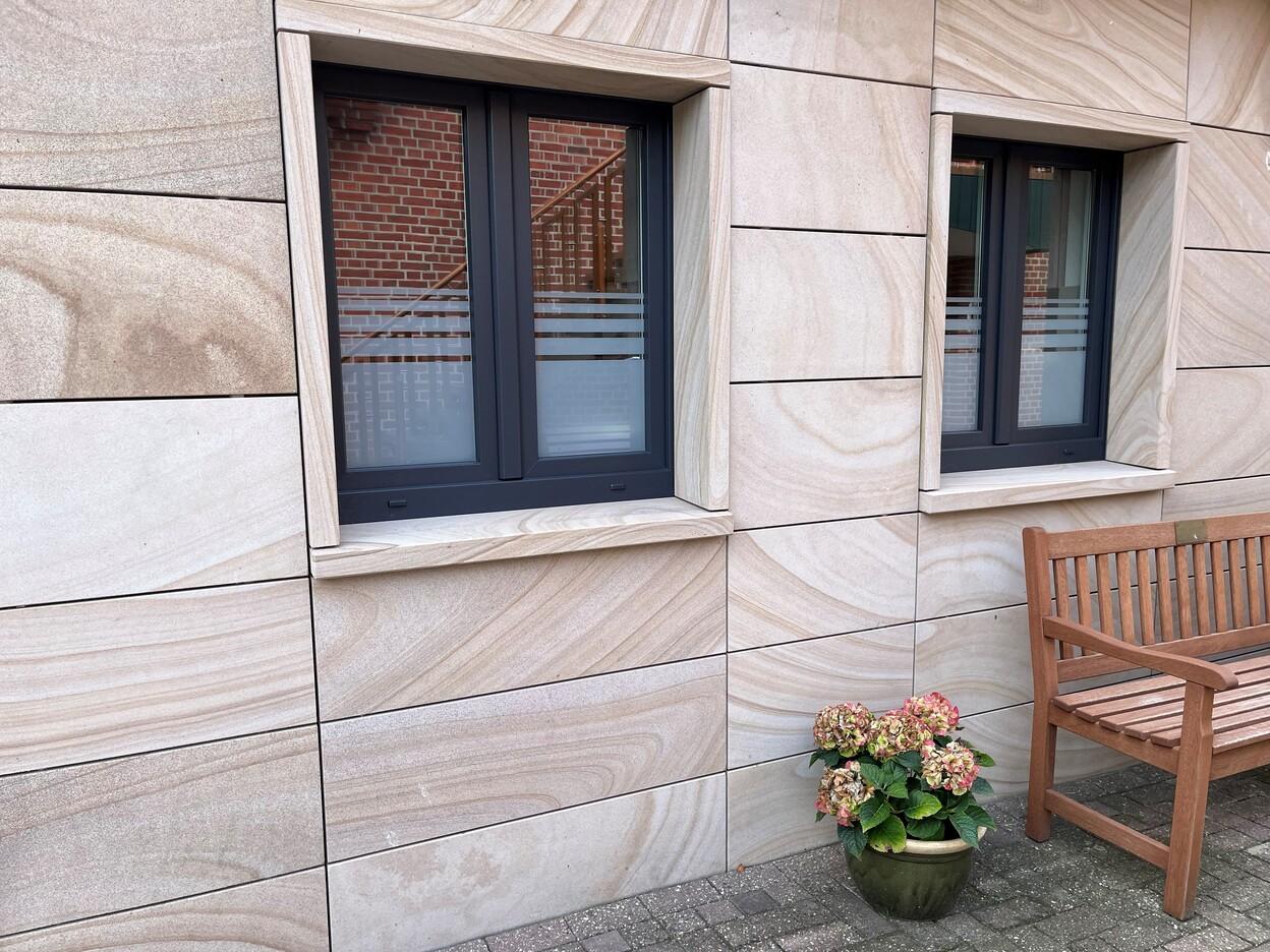 Fenster nach Maß Maßgefertigte moderne Fenster mit schwarzem Rahmen in Sandsteinfassade und Blumendekoration.
