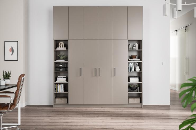 Maßgeschneiderter, multifunktionaler Schrank in Taupe mit integrierten Bücherregalen Ein maßgefertigter, taupefarbener Schrank mit glatten Türen, flankiert von offenen Bücherregalen mit diversen Dekorationsobjekten und Aufbewahrungsboxen.